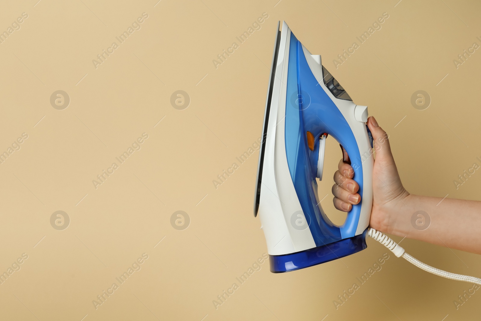 Photo of Woman holding modern iron on beige background, closeup. Space for text