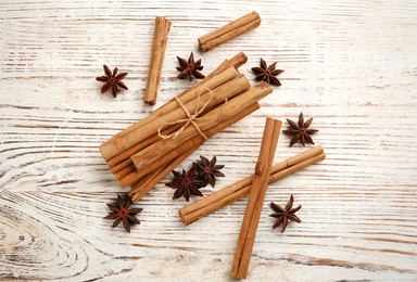 Aromatic cinnamon sticks and anise on white wooden table, flat lay