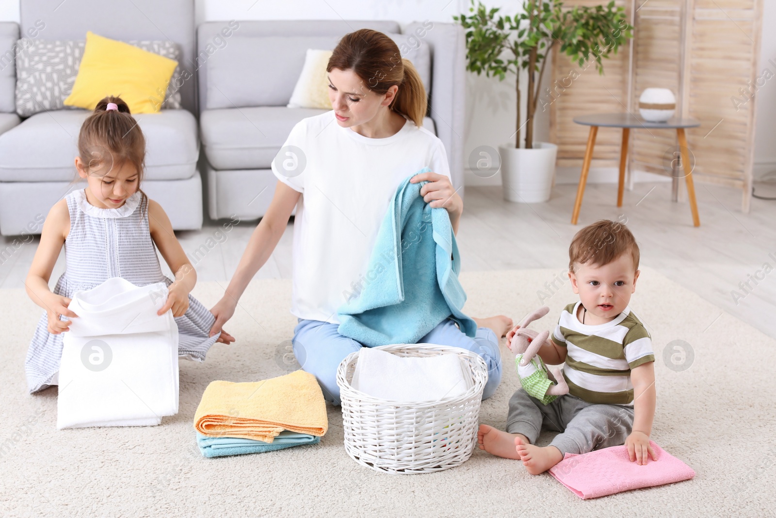 Photo of Housewife with children folding freshly washed towels in room
