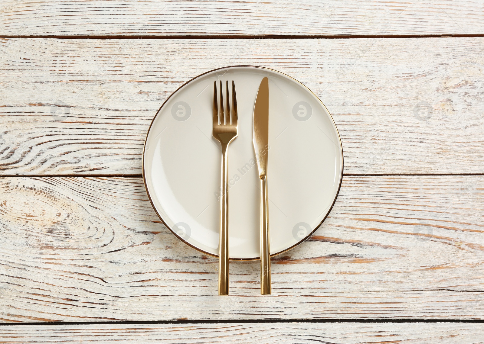 Photo of Beige plate, fork and knife on white wooden table, top view