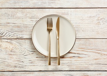 Photo of Beige plate, fork and knife on white wooden table, top view