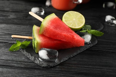 Photo of Slate board with juicy watermelon, ice and lime on black wooden table