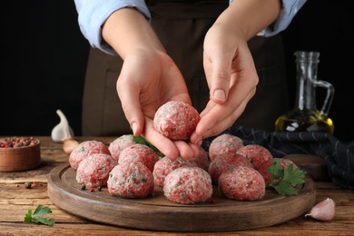 Photo of Woman making fresh raw meatballs at wooden table, closeup