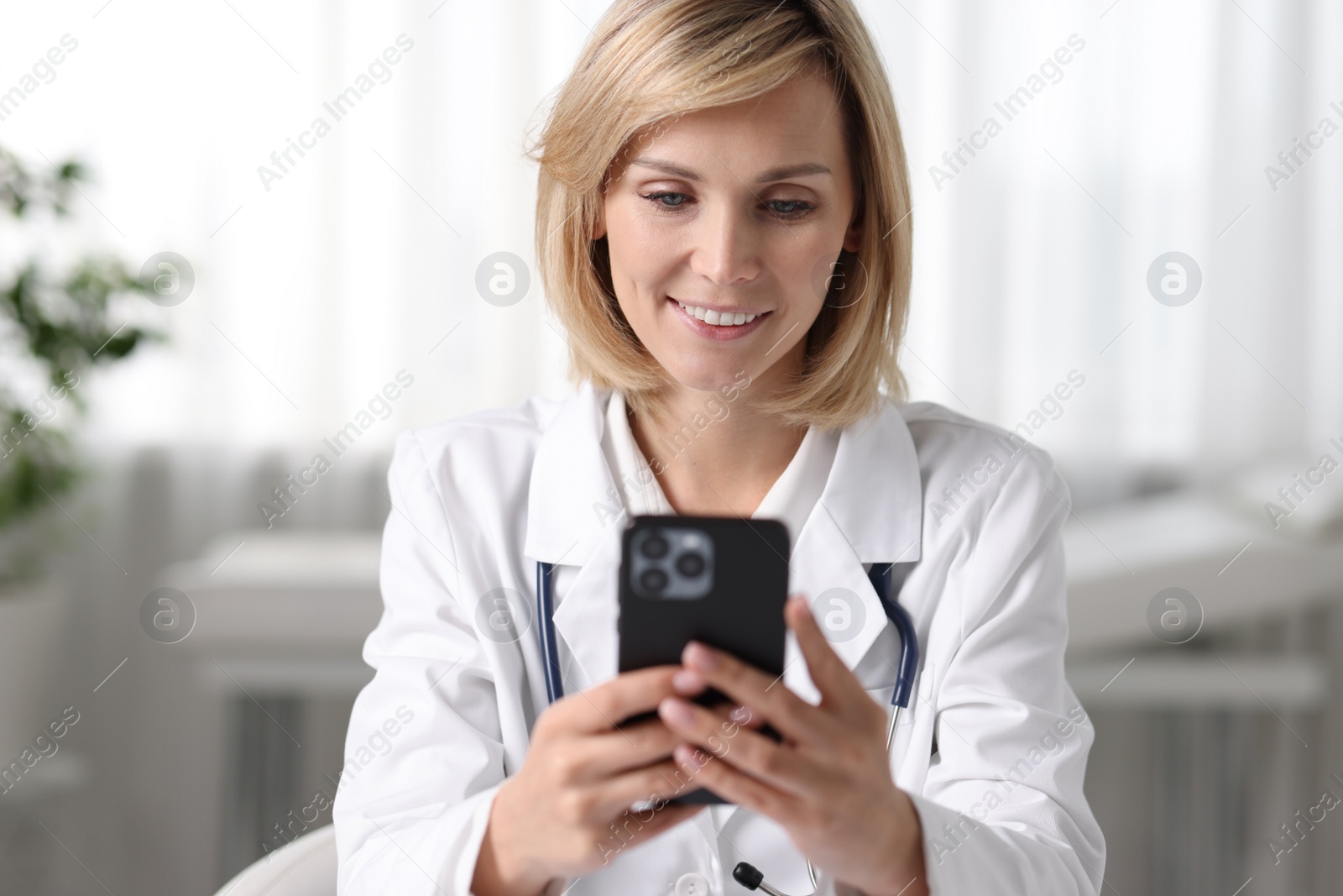 Photo of Smiling doctor with smartphone having online consultation in office