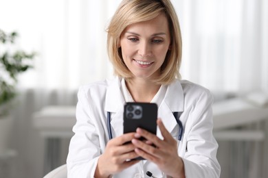 Photo of Smiling doctor with smartphone having online consultation in office
