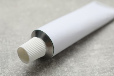 Photo of Blank white tube of ointment on light grey table, closeup. Space for text