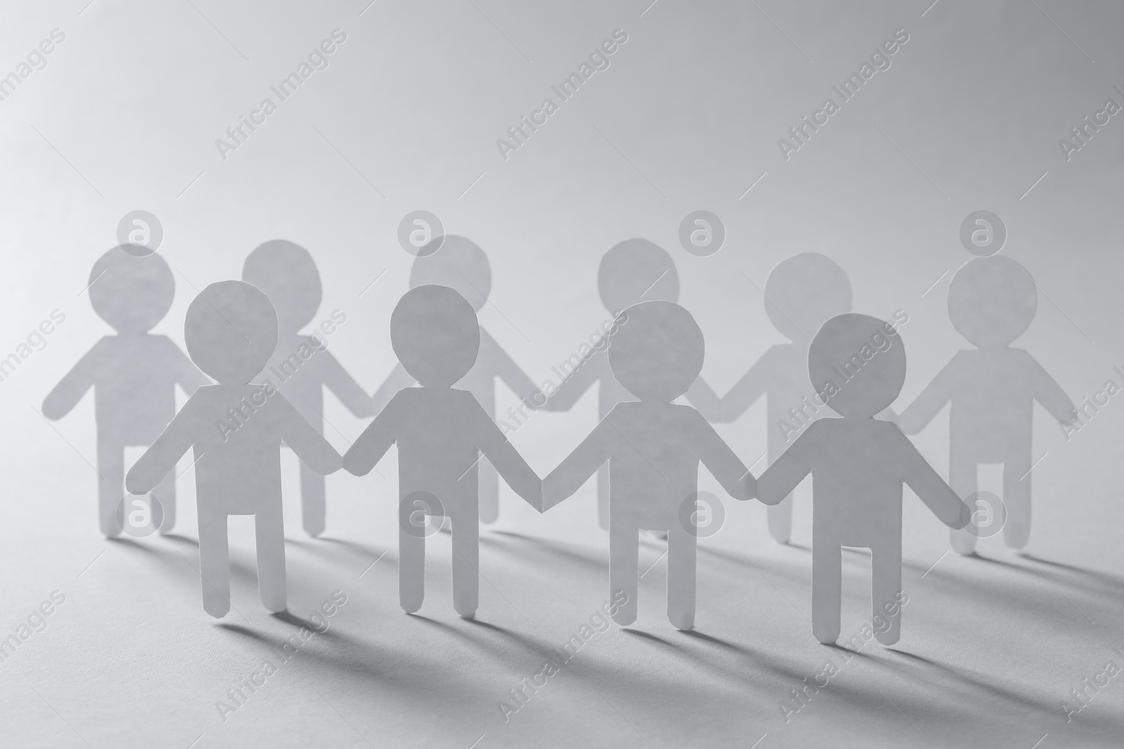 Photo of Teamwork concept. Paper figures of people holding hands on light grey background, closeup