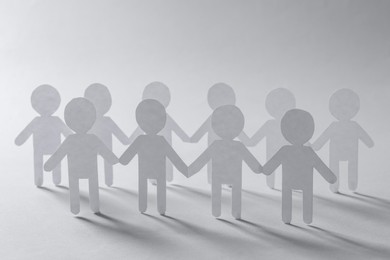 Photo of Teamwork concept. Paper figures of people holding hands on light grey background, closeup
