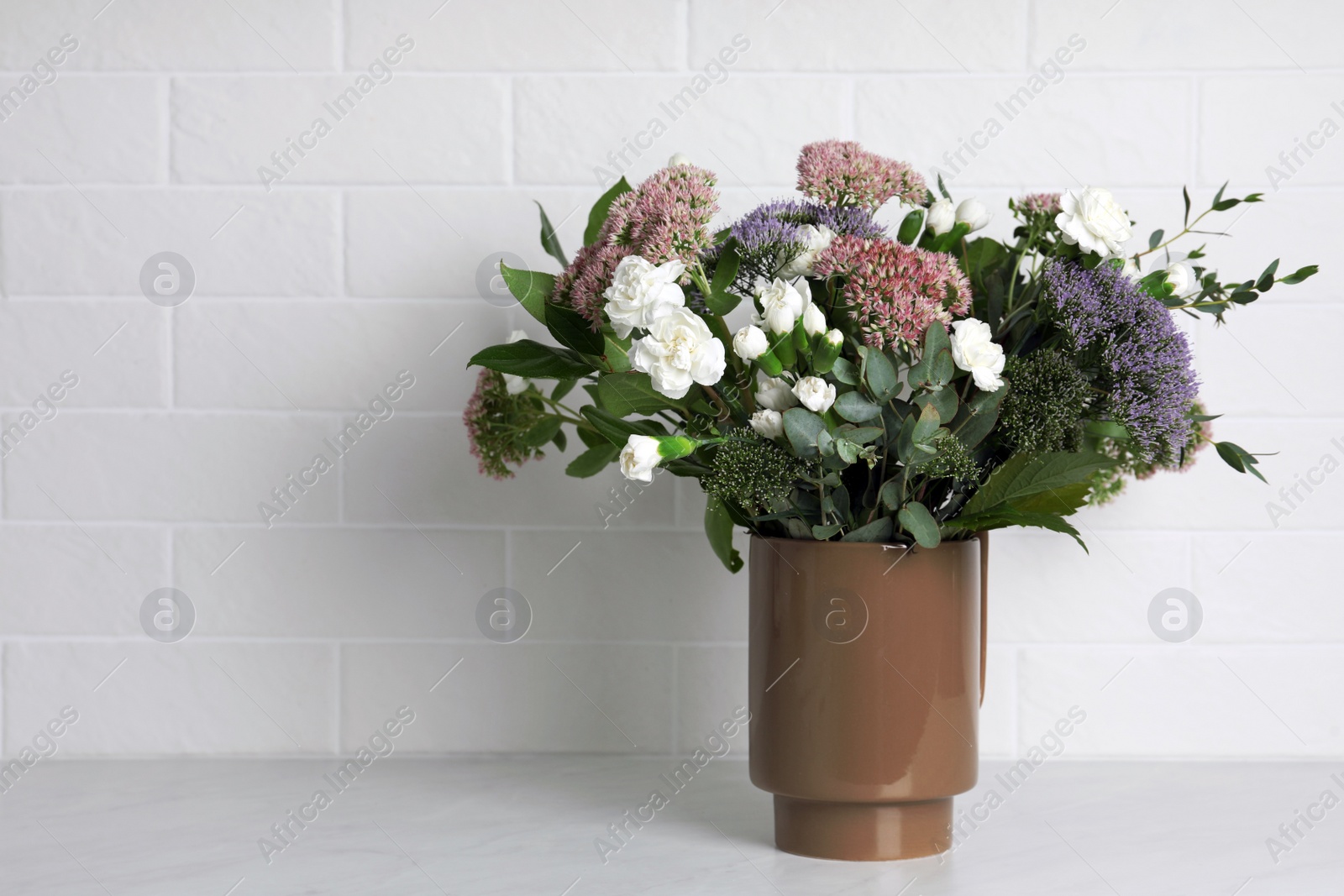 Photo of Ceramic vase with beautiful bouquet on light table near white brick wall. Space for text