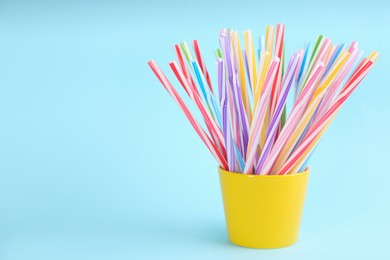 Photo of Colorful plastic drinking straws in holder on light blue background, space for text