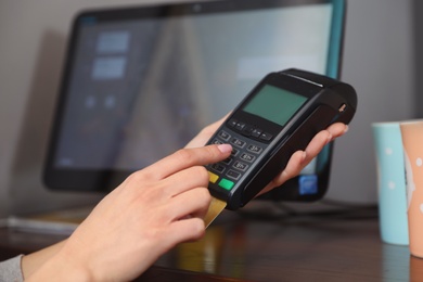 Woman using credit card machine for non cash payment in cafe, closeup. Space for text