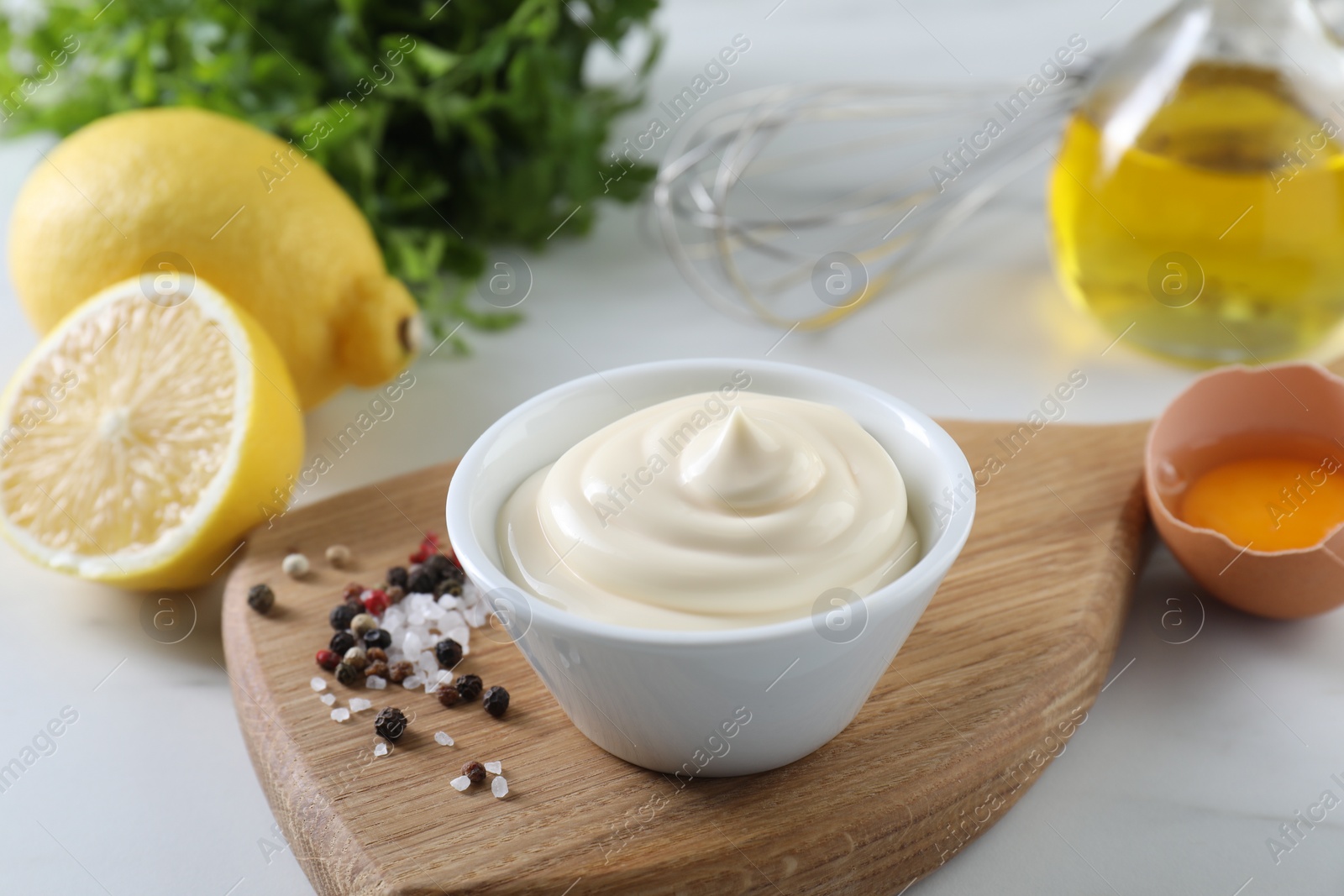 Photo of Tasty mayonnaise sauce in bowl, ingredients and spices on white table, closeup