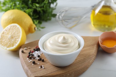 Photo of Tasty mayonnaise sauce in bowl, ingredients and spices on white table, closeup