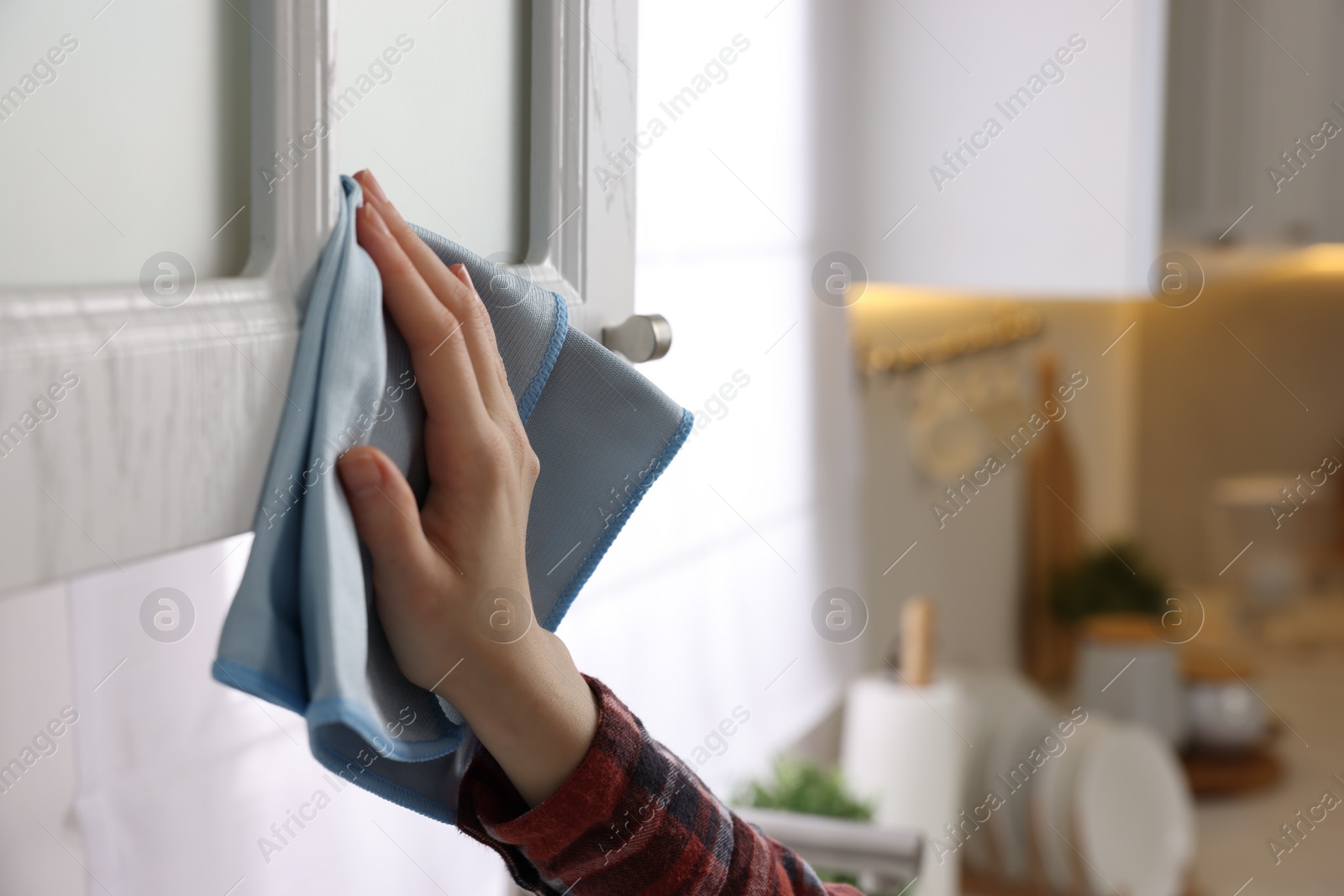 Photo of Woman with microfiber cloth cleaning white cabinet in kitchen, closeup