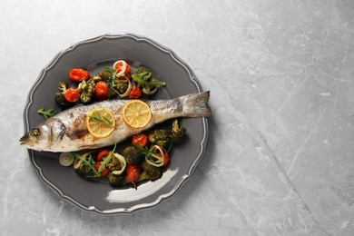 Photo of Baked fish with vegetables and lemon on grey textured table, top view. Space for text