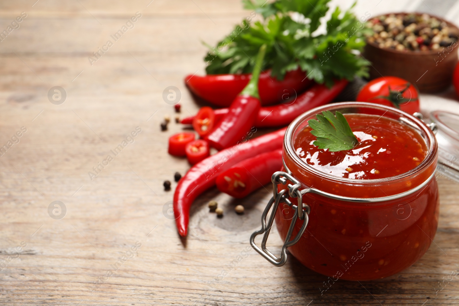 Photo of Spicy chili sauce in glass jar on wooden table. Space for text