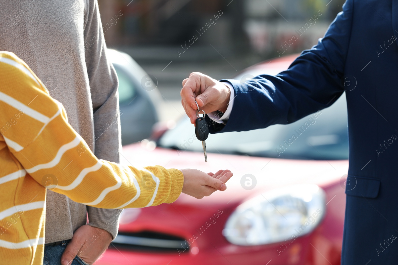 Photo of Salesman giving key to customers in modern auto dealership, closeup. Buying new car