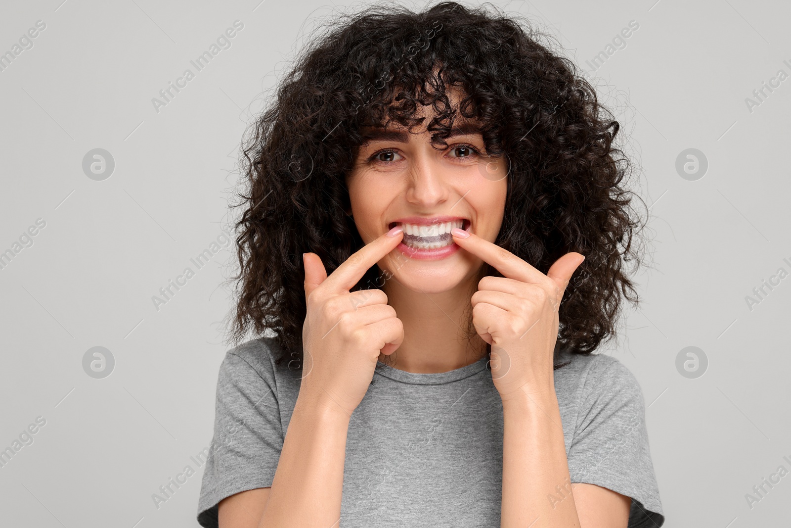 Photo of Young woman applying whitening strip on her teeth against light grey background