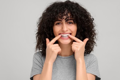 Photo of Young woman applying whitening strip on her teeth against light grey background