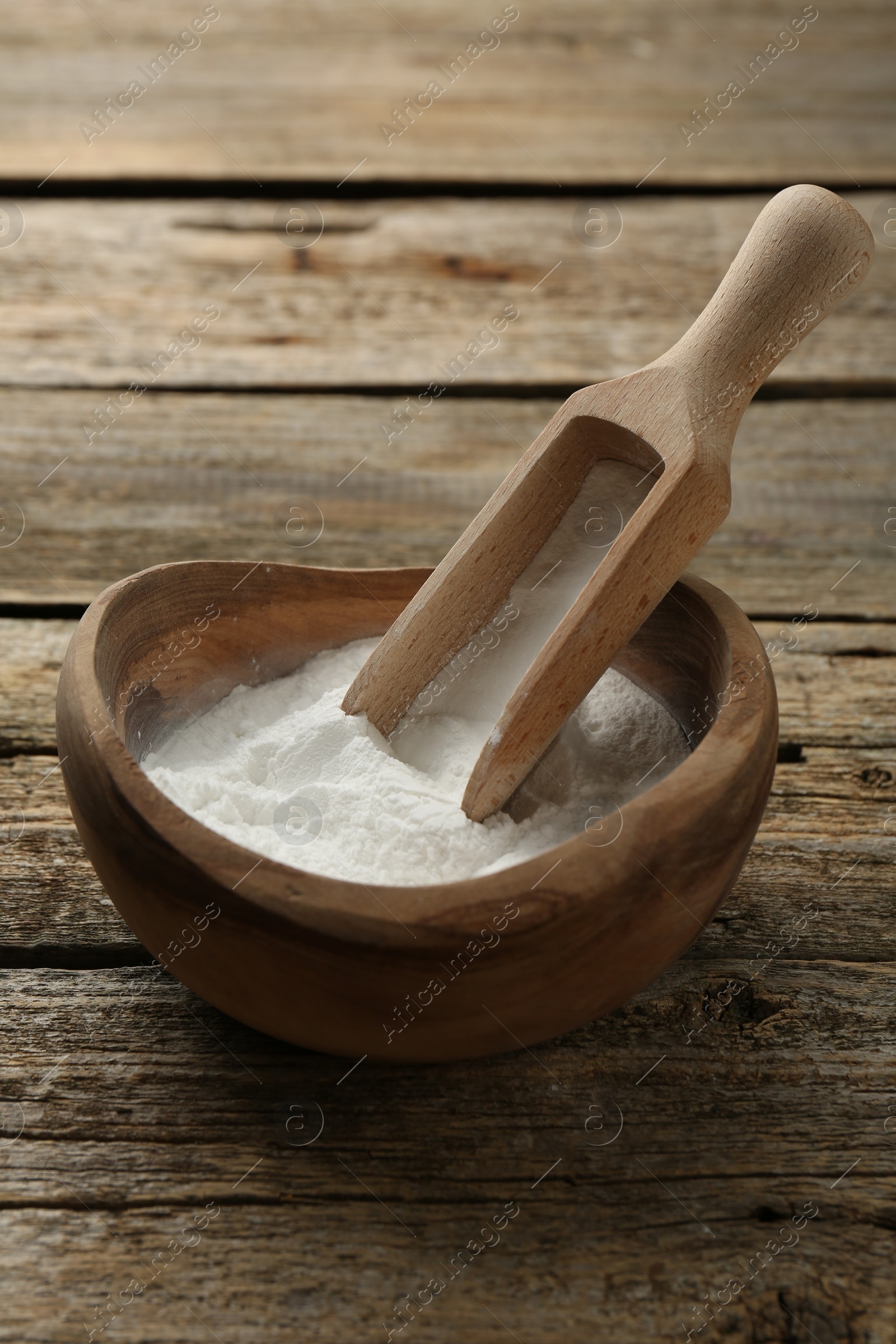 Photo of Baking powder in bowl and scoop on wooden table