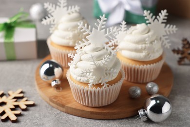 Tasty Christmas cupcakes with snowflakes and festive decor on grey table