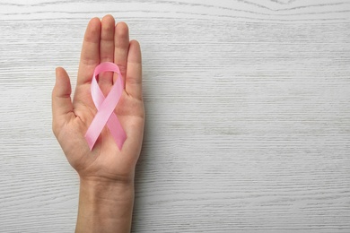 Woman holding pink ribbon on wooden background, top view with space for text. Breast cancer awareness concept