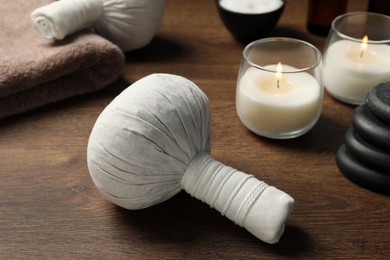 Photo of Herbal massage bags, spa stones and candles on wooden table, closeup