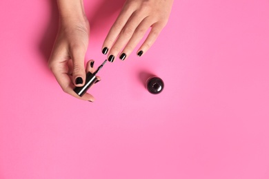 Woman applying nail polish on color background, top view with space for text