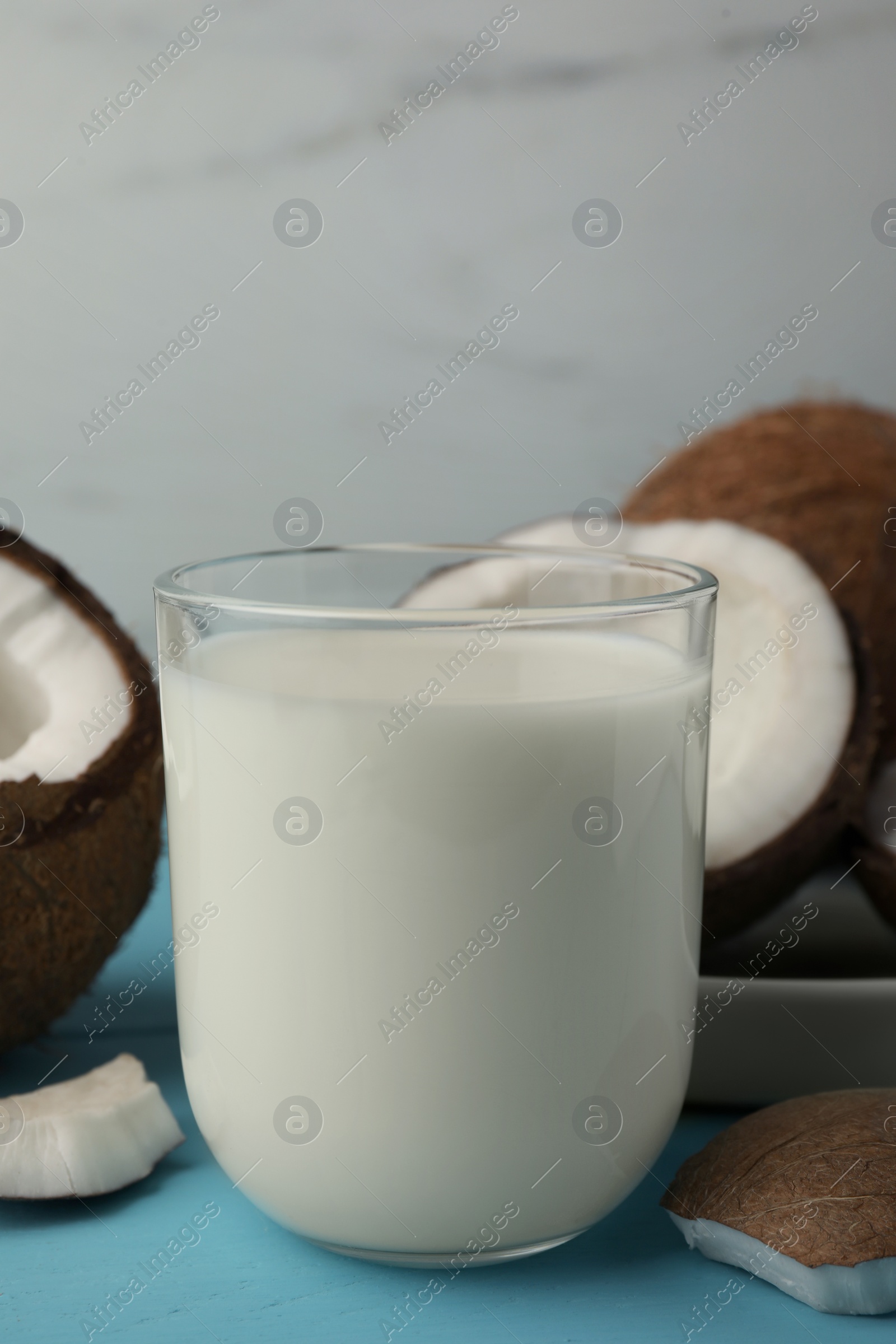 Photo of Glass of delicious vegan milk and coconuts on light blue wooden table