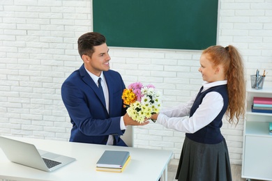 Photo of Schoolgirl congratulating her pedagogue with bouquet in classroom. Teacher's day