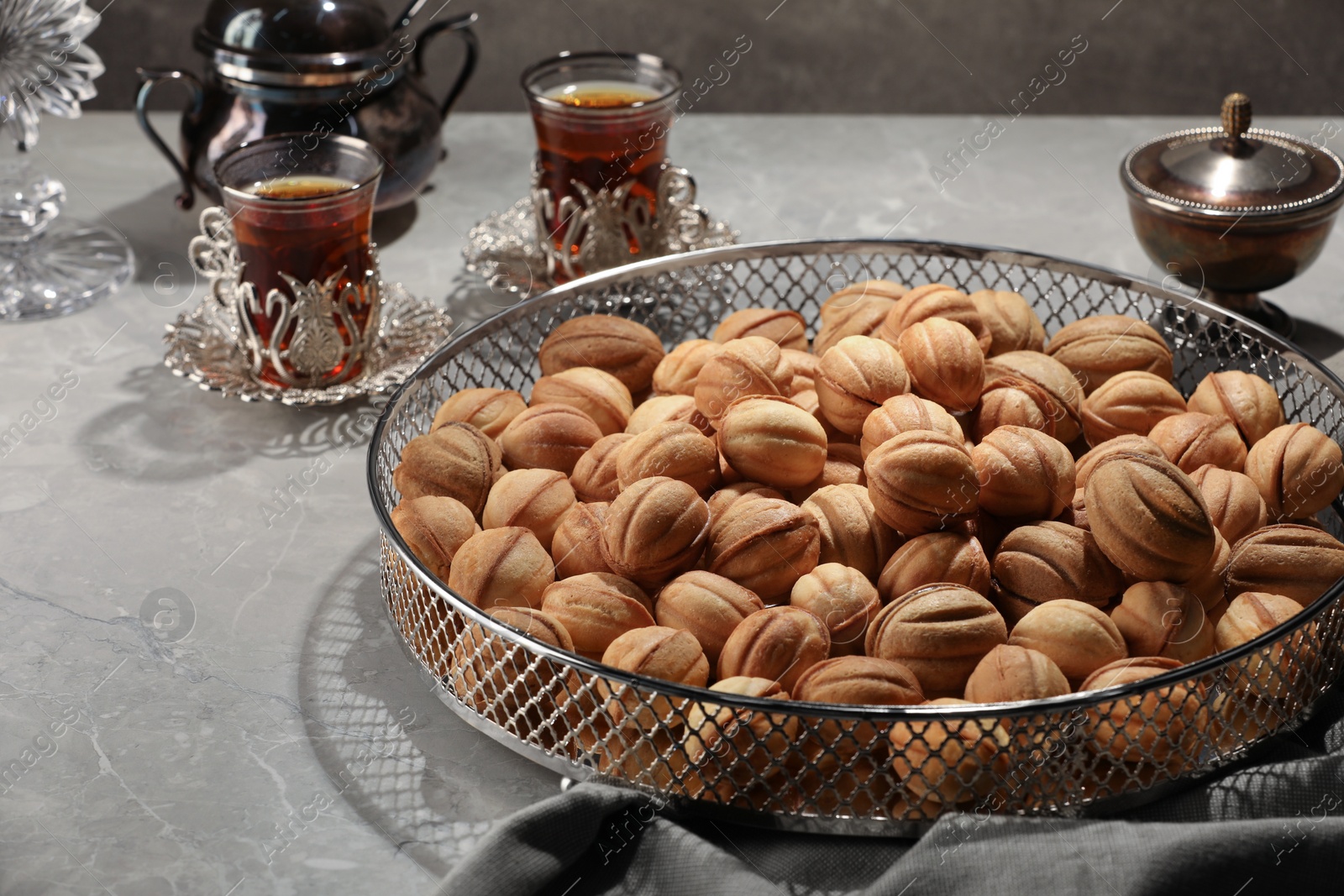 Photo of Delicious walnut shaped cookies and glasses of tea on grey table, closeup. Tasty pastry with filling carrying nostalgic home atmosphere