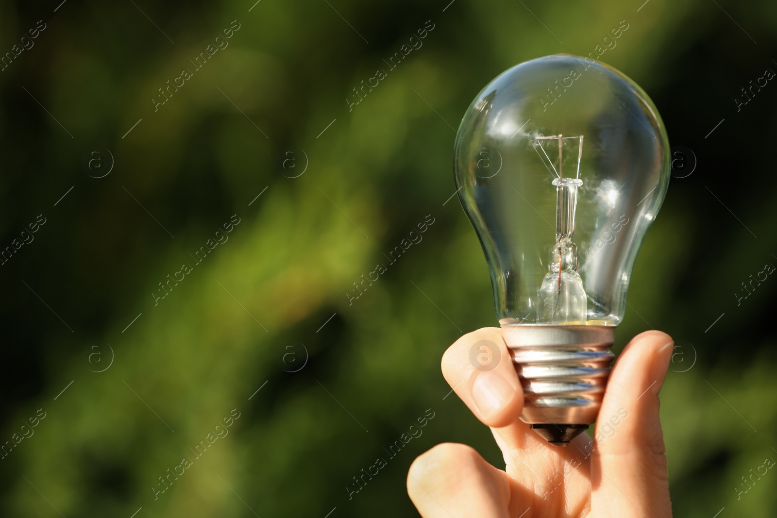 Photo of Woman holding incandescent light bulb on blurred green background, closeup. Space for text