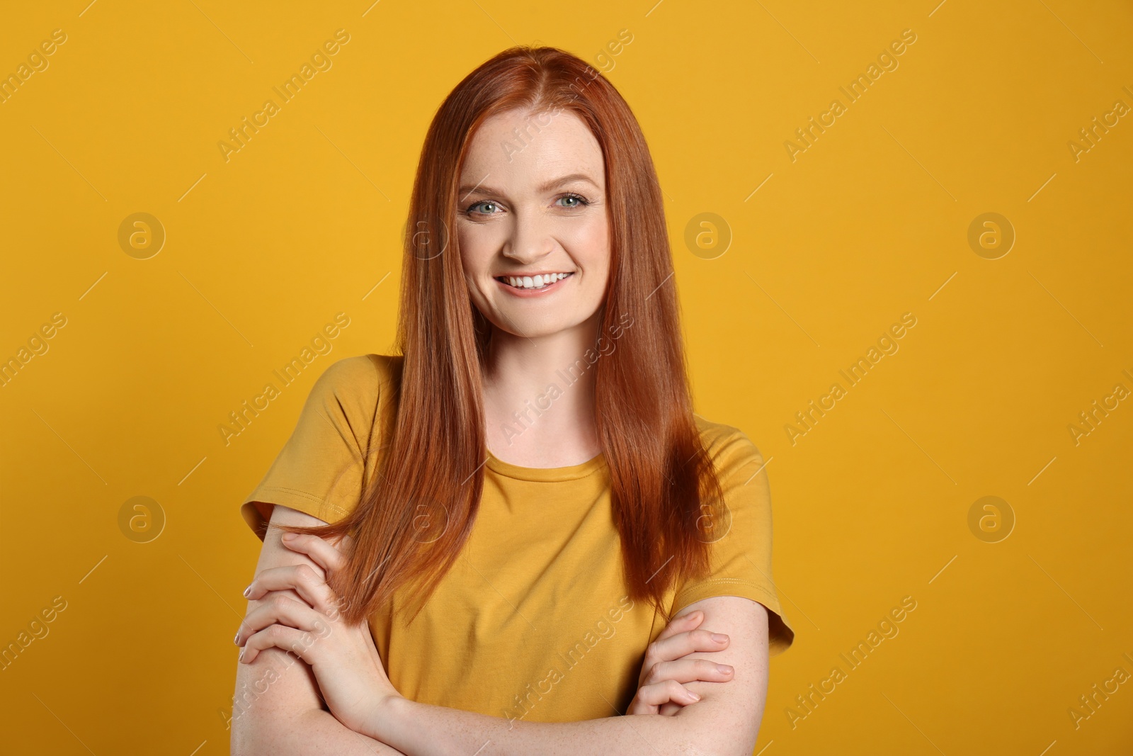 Photo of Candid portrait of happy young woman with charming smile and gorgeous red hair on yellow background