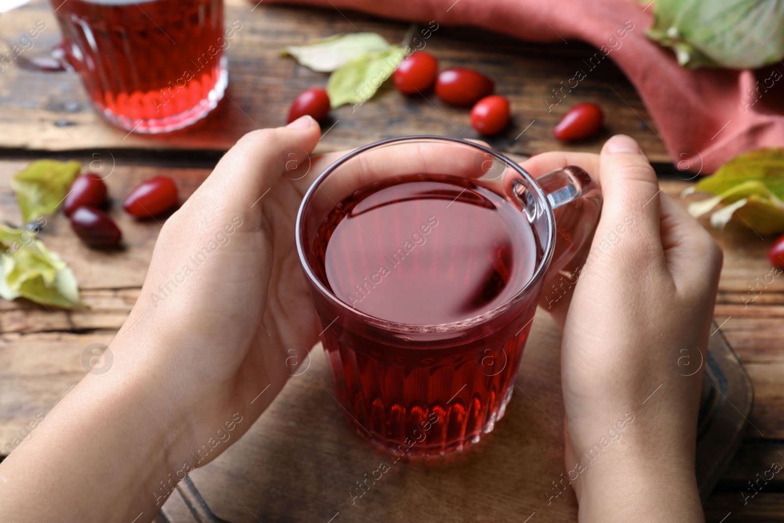 Photo of Woman with cup of fresh dogwood tea at wooden table, closeup