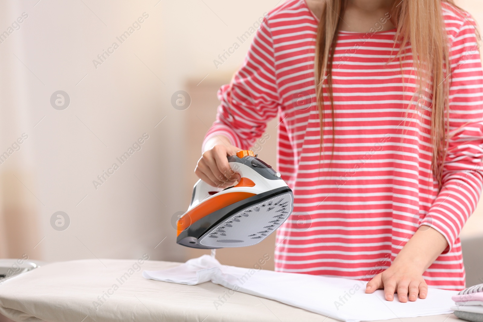 Photo of Young woman ironing clean laundry on board indoors, closeup. Space for text