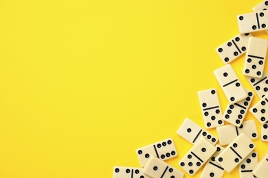 Photo of Classic domino tiles on yellow background, flat lay. Space for text