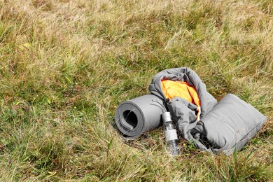 Grey sleeping bag, camping mat and bottle on green grass outdoors, space for text