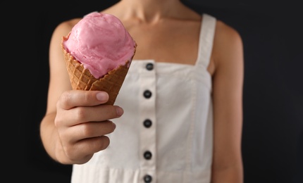 Photo of Woman holding pink ice cream in wafer cone on black background, closeup