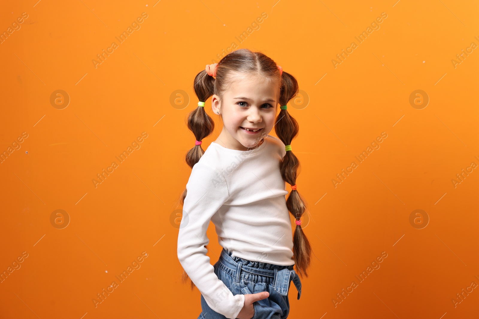 Photo of Cute little girl with beautiful hairstyle on orange background