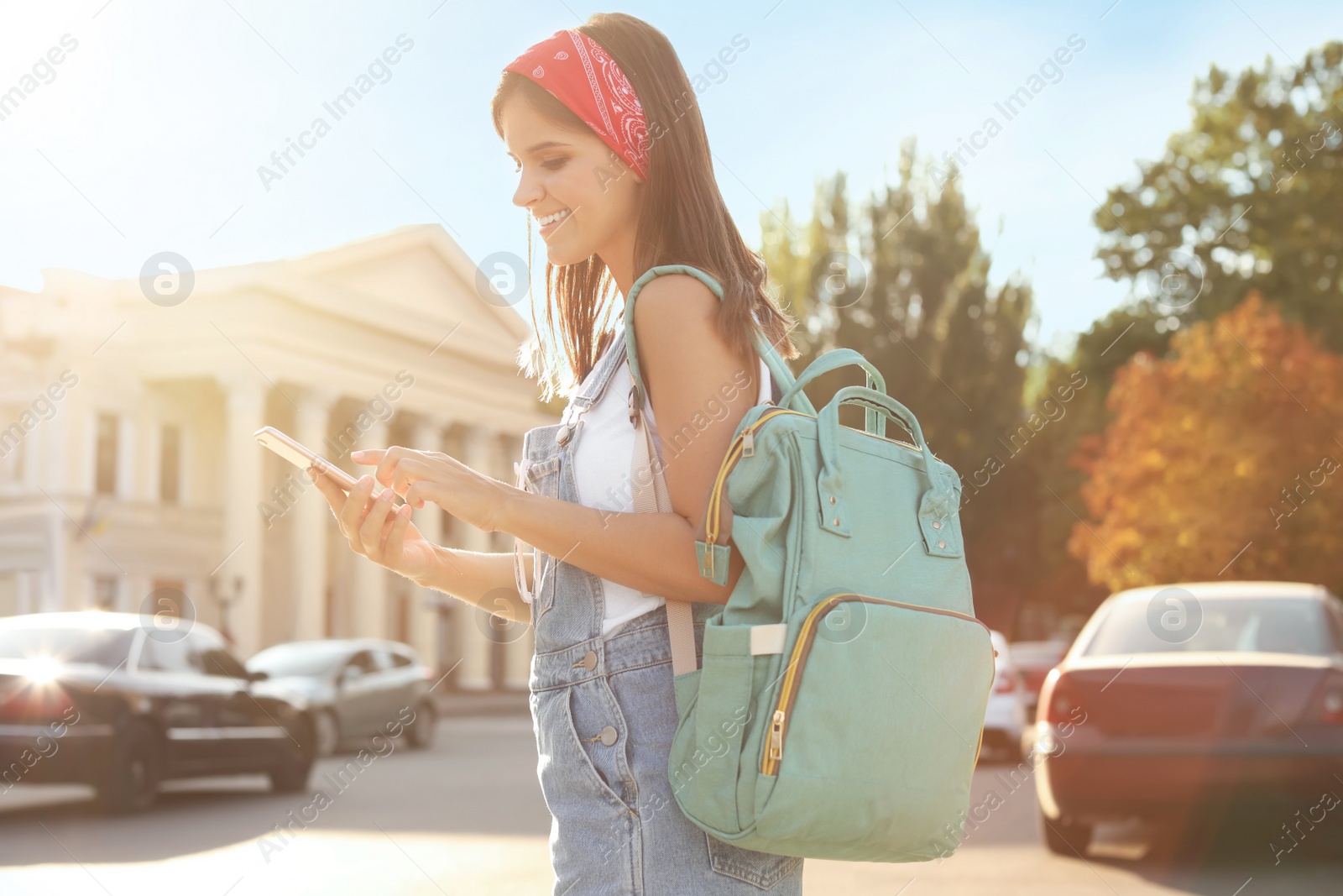 Photo of Young woman with stylish turquoise bag and smartphone on city street