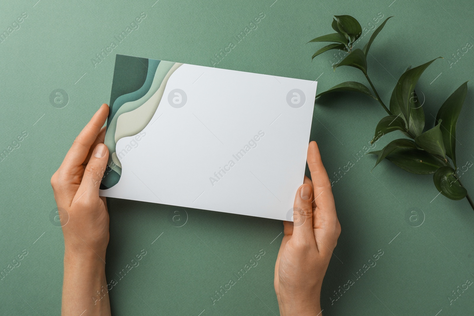 Photo of Woman holding blank invitation card on green background, top view. Space for text