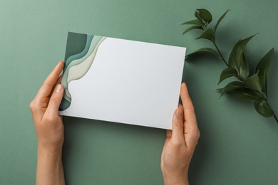 Woman holding blank invitation card on green background, top view. Space for text