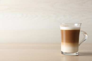 Photo of Hot coffee with milk in glass cup on wooden table. Space for text