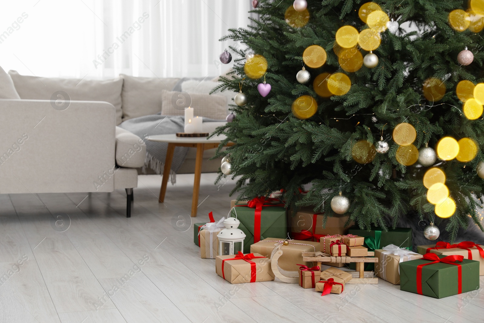 Photo of Beautifully wrapped gift boxes, wooden sleigh and lantern under Christmas tree in living room