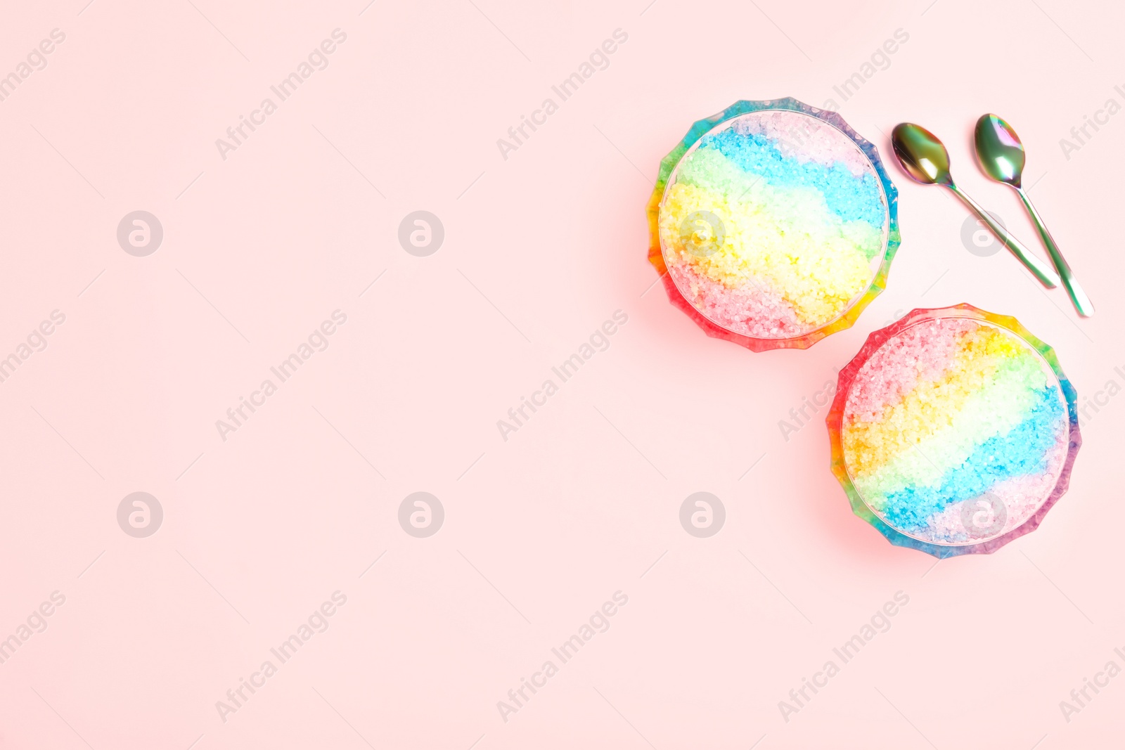 Photo of Rainbow shaving ice in glass dessert bowls and spoons on light background, flat lay. Space for text