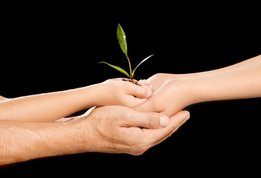 Photo of Family holding soil with green plant in hands on black background