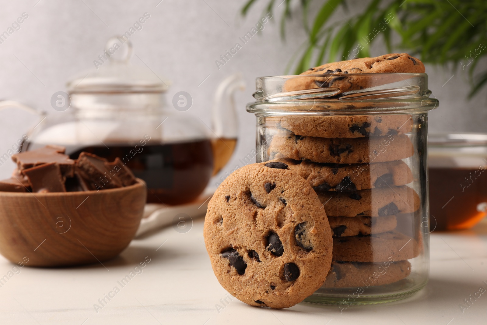 Photo of Glass jar with delicious chocolate chip cookies and tea on white marble table