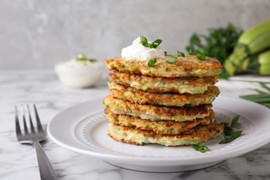 Photo of Delicious zucchini fritters with sour cream served on white marble table, closeup