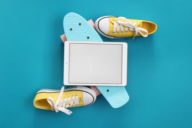 Modern tablet, skateboard and shoes on light blue background, flat lay. Space for text