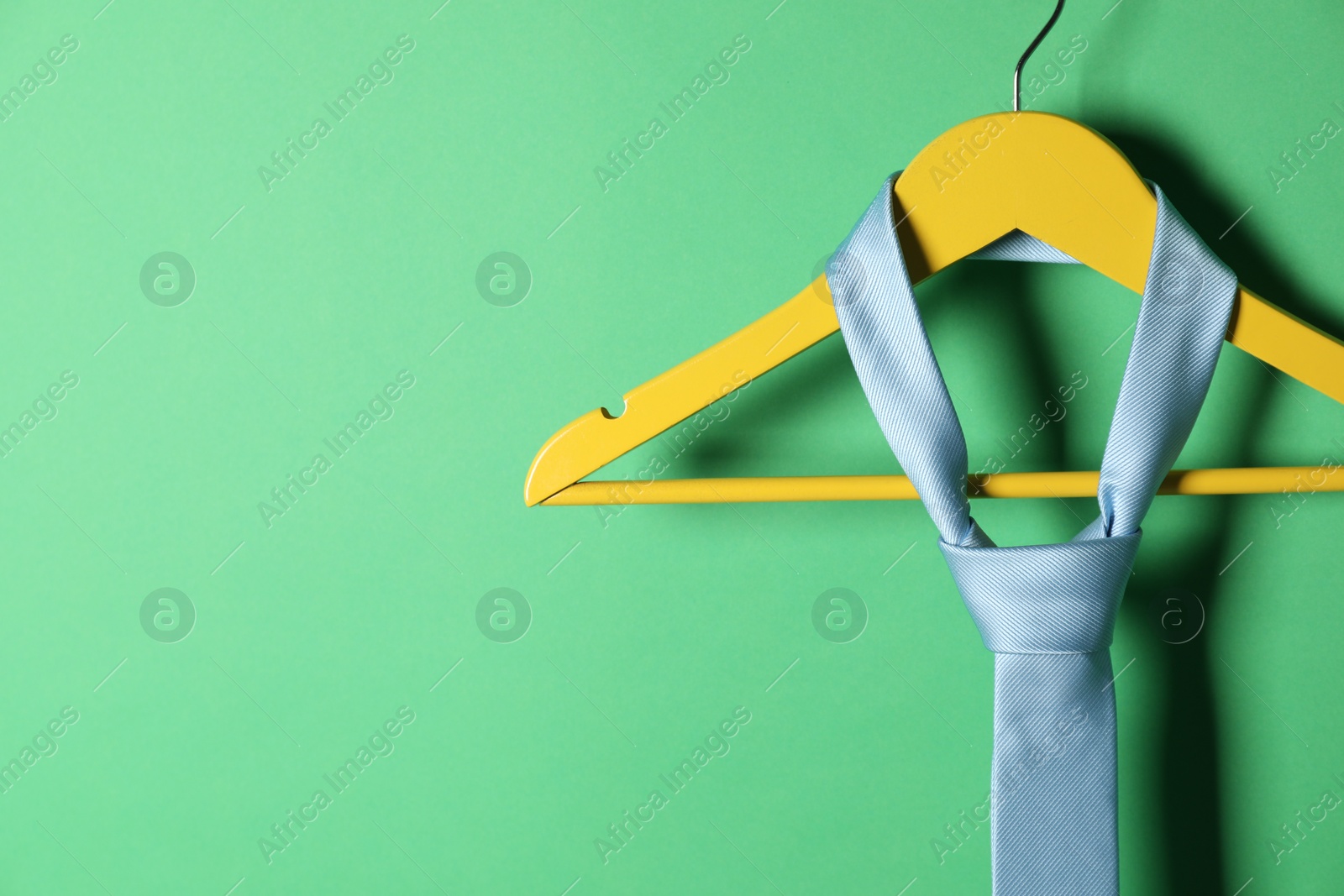 Photo of Hanger with light blue tie on green background, closeup. Space for text